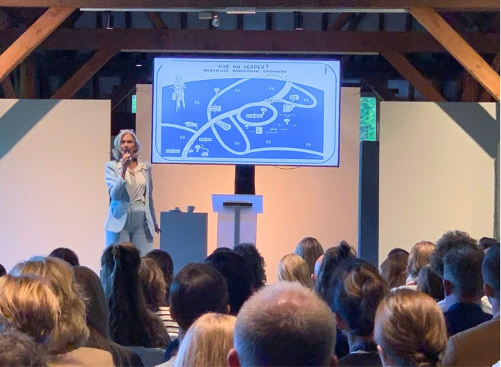 Anja op het podium voor een volle zaal.